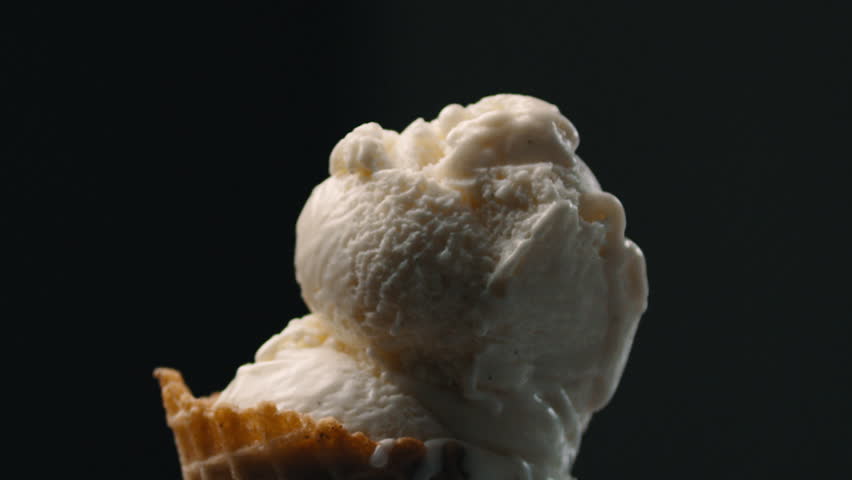 Crunchy flakes sprinkled over vanilla ice cream in cone black background