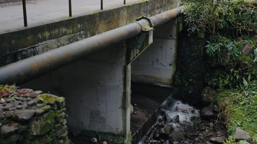 Old bridge, iron pipeline and water flowing outdoors. Water stream on street