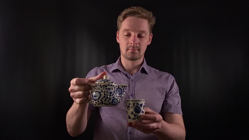 Stylish portrait of a trendy young man pouring a hot drink. Dressed in a vibrant purple shirt he exudes an effortlessly cool demeanor on the black backdrop. Lifestyle, beverage or fashion