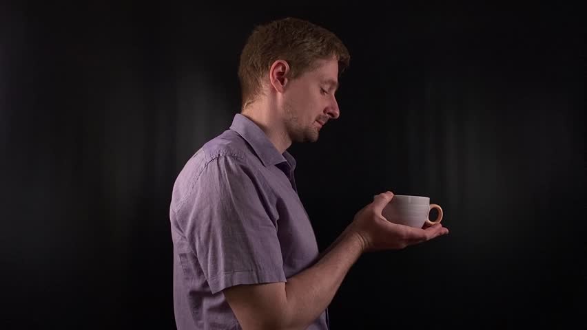 Stylish portrait of a trendy young man sipping a hot drink. Dressed in a vibrant purple shirt he exudes an effortlessly cool demeanor on the black backdrop. Lifestyle, beverage or fashion