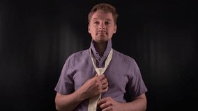 Dapper portrait of a stylish young man adjusting a crisp white necktie. Clad in a vibrant purple shirt with casual stubble he exudes an effortlessly cool yet refined vibe on the minimal black backdrop - Powered by Shutterstock - Get 15% off with code: PIKWIZARD15