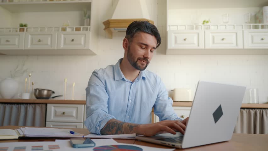 Smiling businessman working at home. Portrait of young happy businessman manager entrepreneur working typing on laptop computer, looking at camera and smiling. Enjoy work, solution, efficient concept.