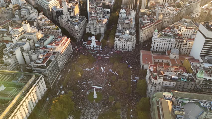 Crowd of Argentinian Young Protester on Plaza de Mayo in Buenos Aires at golden hour. Students on street at anti-government march at sunset. Waving Argentinian Flag at square. People on demonstration.