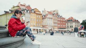 Elderly woman sitting on the steps of the monument, drinking coffee and looking at a smartphone at Palace Square in Warsaw, Poland, Slow motion - Powered by Shutterstock - Get 15% off with code: PIKWIZARD15