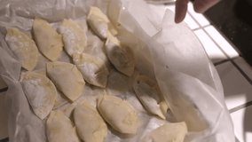This video shows a hand placing taking home made dumpling wontons and putting them in a boiling pot for cooking. 