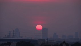 Footage of red sun sets behind the silhouette of city buildings, sunset