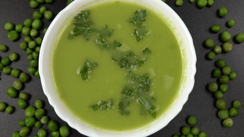 Adding of white sesame seeds  to fresh green pea puree soup in a white bowl standing  on a black table