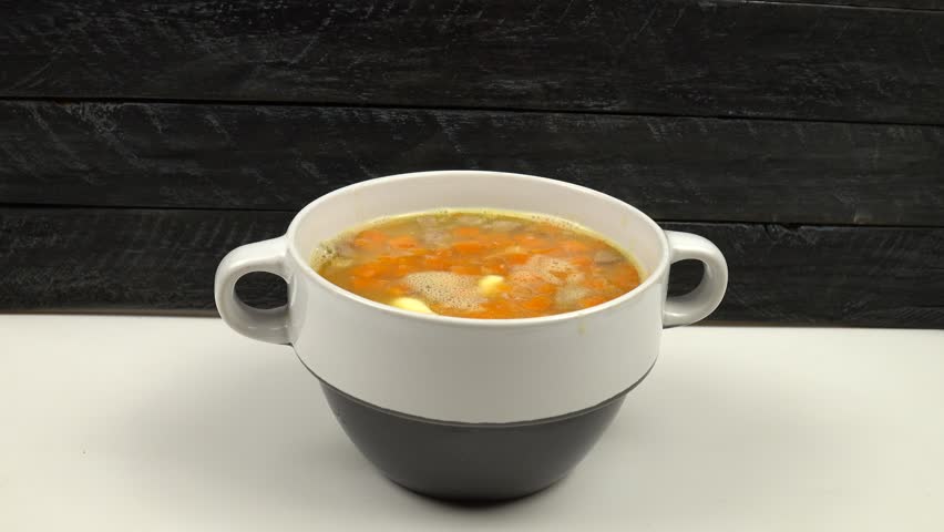 Adding of chopped parsley to hot pea soup in a ceramic bowl. A bowl of hot pea soup stands on the kitchen table on a black background