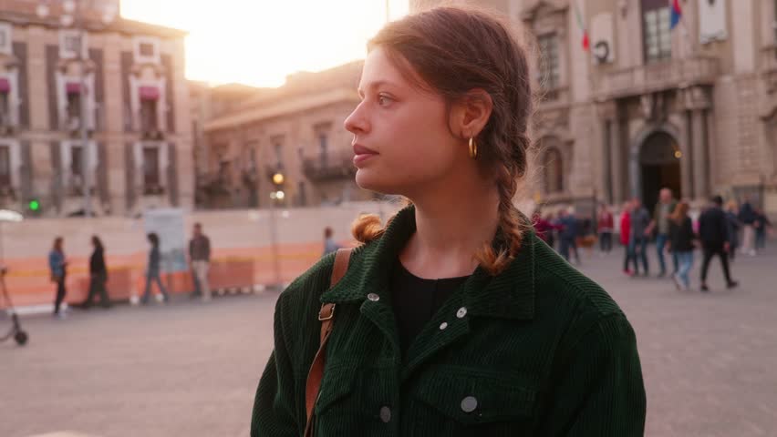 Young brunette woman walks through the streets of the city of Catania in Sicily, Italy, among the sunset lights with vintage clothes.