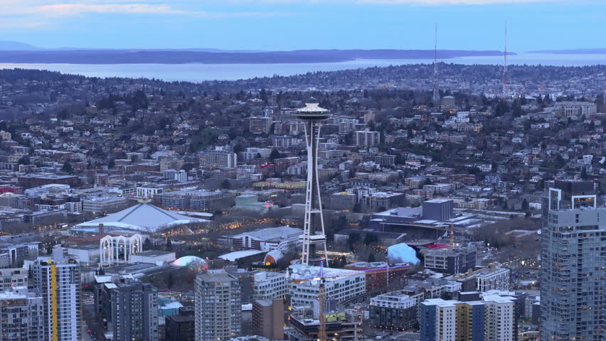 An expansive aerial view of the Seattle skyline with the iconic Space Needle standing tall amid residential and commercial buildings as evening approaches. 4K footage. 