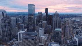 An aerial view captures the twilight essence over Seattles urban landscape, highlighting reflective skyscrapers and distant mountain ranges. City vibrancy meets natural tranquility. 4K footage. 