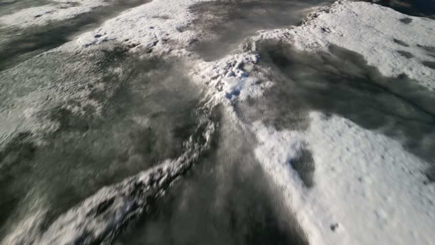 Fast low aerial looking down on frozen lake in Colorado Rocky Mountains in springtime