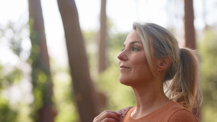 Mature woman on hike in countryside closing eyes and breathing deeply enjoying calm of nature - shot in slow motion