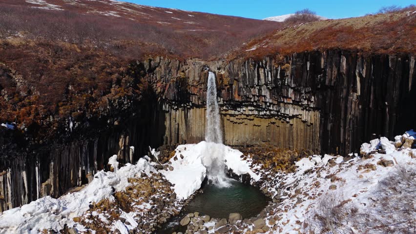 Small Waterfall cascades into frozen lake, geological formation after eruption