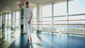 Boyfriend shoot video from training for girlfriend, hip-hop dancer energetically moving for camera. Handsome tattooed guy wearing white sport clothes in hall with big windows. Concept of choreographic