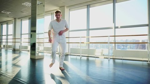 Choreographer select moves for new hip-hop dance, boy with mustache training with group. Tattooed barefoot guy wearing white T-shirt and trousers. Concept of sportswear, dancing school or hall for