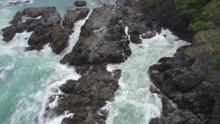 A rocky shoreline with a large body of water in the background. The waves are crashing against the rocks, creating a powerful and dynamic scene. The rocks are scattered throughout the area