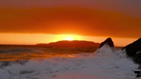 Beautiful video of a red sunset during a storm on the Adriatic Sea in Rafailovici, Montenegro. Huge waves of the raging sea. In the foreground the sky is overcast.