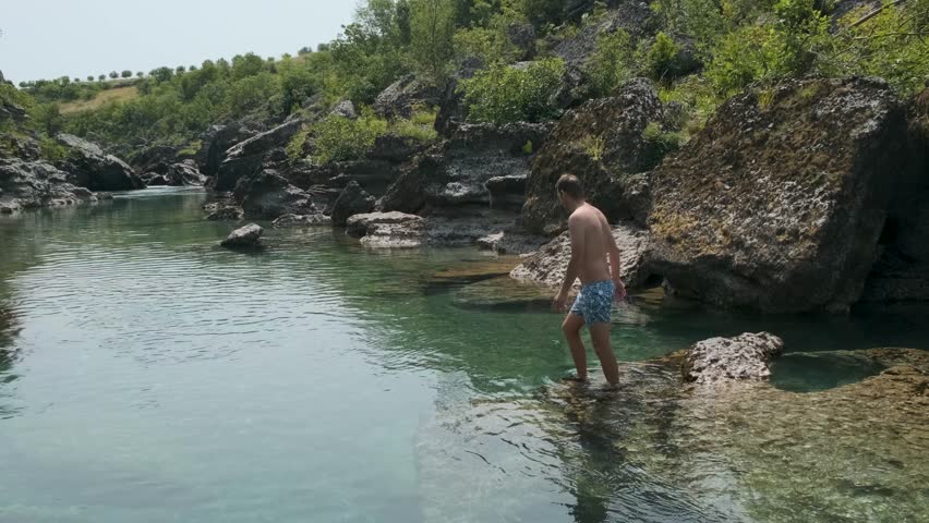 Man jumping into the canyon river with crystal clear blue water for refreshing in hot summer day on vacations. Caucasian male diving in cold river water to swim, having fun