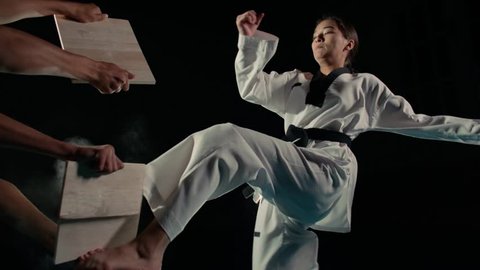 Asian beautiful girl fighter practicing to break the board with a kick of the feet, slow motion
