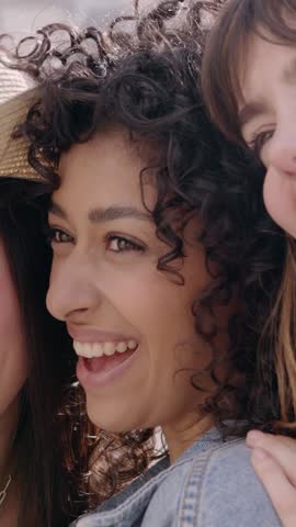 Vertical close up video portrait of three young smiling women laughing together outdoors. Diverse female friends having fun together on summer vacation. Youth lifestyle and friendship concept. 