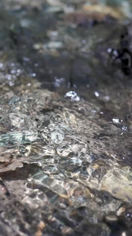 Vertical screen of flowing clean transparent water in a mountain stream or river in slow motion. Drinking clean water flows from a natural mountain spring. Fresh water reserves on the planet