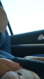 A video showcasing a young boy sitting in a car seat, wearing sunglasses and a hat. Vertical footage.