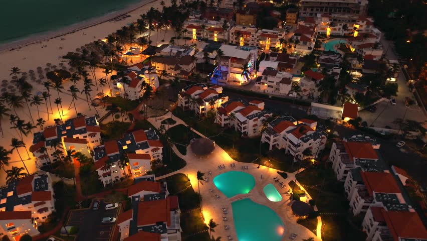 Aerial view of popular tourist coastal city at night. A luxurious tourist hotel with a lighted pool. The flickering city lights below create a mesmerizing view. Punta Cana, Dominican Republic
