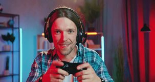 Close up portrait of man gamer in earphones which enjoying his victory in video games at home in contemporary night room