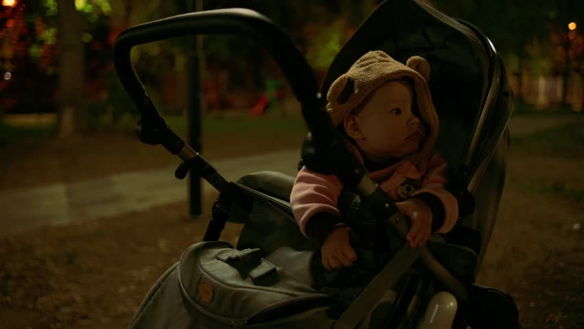 Portrait of a cute toddler girl in a stroller in the park at night