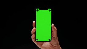 Smartphone with chroma key screen on black background close-up. Green screen on mobile phone in hand.