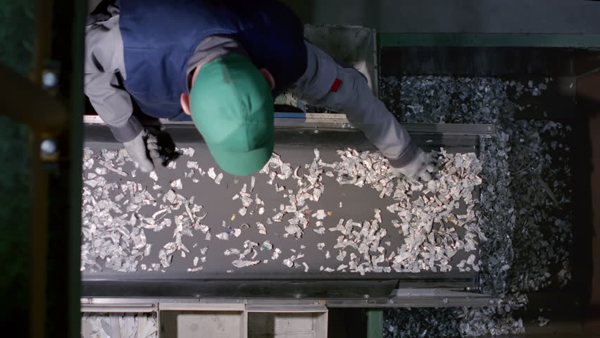 Man removes non-recyclable items ensuring necessary particles continue moving on belt slow motion. Worker ensures valuable materials salvaged and recycled contributing to more sustainable future