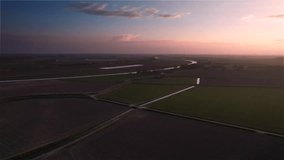 The evening sun casts a warm glow over a flat, empty stretch of Dutch farmland, accompanied by a dike.