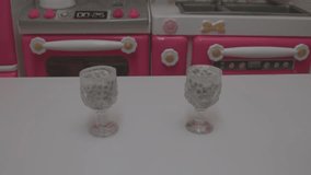 macro video showcases a child's toy kitchen set with a pink oven and accessories, with hands preparing food in miniature dishes.