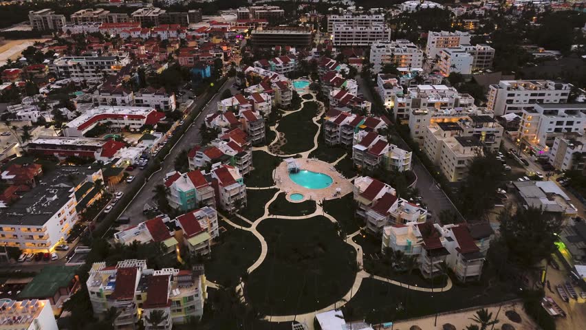 An aerial twilight view of a popular coastal tourist city, featuring a luxurious hotel with a lit pool amidst mesmerizing city lights below. This is Punta Cana, Dominican Republic