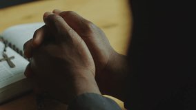 Clasped hands of unrecognizable Black clergyman leaning on wooden table with opened Bible book while praying. Close-up view - Powered by Shutterstock - Get 15% off with code: PIKWIZARD15