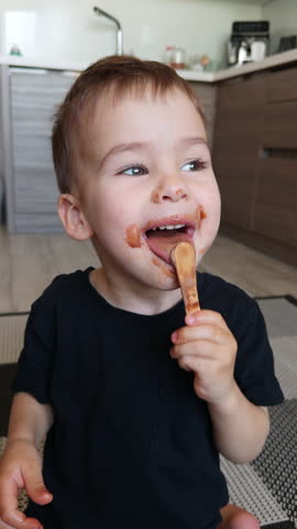 Happy smiling baby holding a wooden stick from an ice cream. Cute kid finishing chocolate ice-cream. Close up. Vertical video.