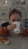Caucasian toddler drinking from paper cup. Funny kid with foam moustache after drinking cocoa. Vertical video.