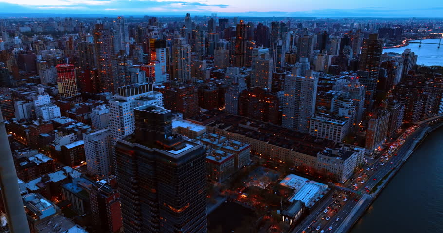 Business center of New York turning on lights at twilight. Drone flies above the highway with busy traffic on the shore of the East River.