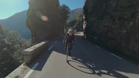 Slow motion action camera shot of inspiring female athlete, overcomes fear and sexism climbs up mountain road on professional racing carbon bicycle, looks determined and powerful