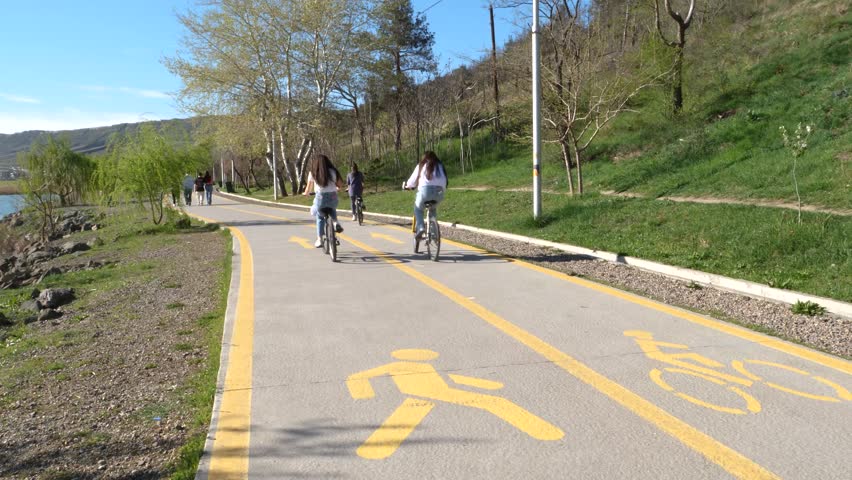 A pair of teenage girls enjoying a leisurely bike ride along a designated path in a park with clear signage.