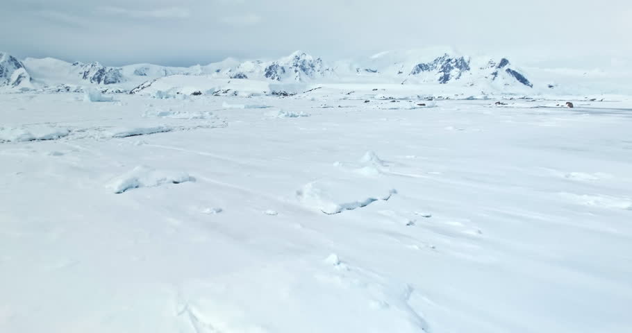 Fly above frozen panorama of Antarctic Peninsula. Desert white land of snow mountains and ice drone shot. Antarctica travel exploration. Discover beauty of South Pole. Wild nature winter background