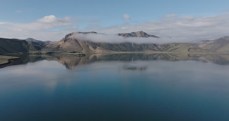 Aerial Backward Tranquil Shot Of Rock Formations And Lake Under Clouds On Sunny Day - Unknown, Iceland