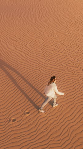 Vertical video. A person standing alone in the vast expanse of a desert, surrounded by sand dunes under a clear sky.