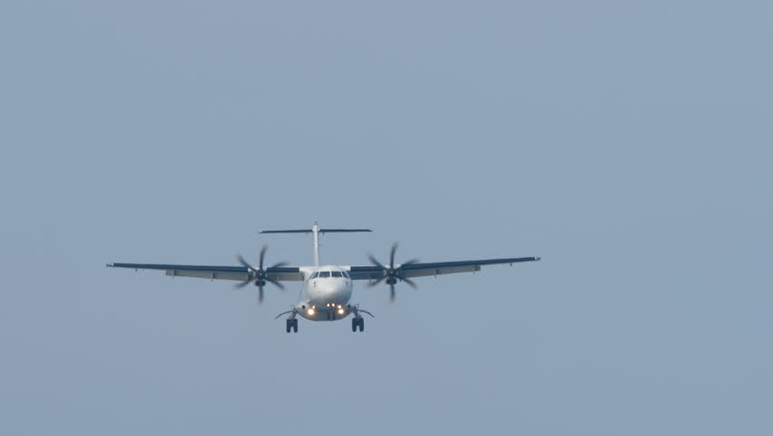 Front view of a turboprop airplane with an unrecognizable livery flying, descending for landing. Twin-engine short-haul regional passenger aircraft. Blue background.