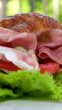 croissant sandwich with meat jamon prosciutto with tomato Lettuce leaves vegetables natural healthy expensive food rich pieces of cheese in breakfast France on a white plate. expensive restaurant