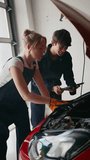 Vertical video portrait of team of car mechanics with male and female trainees holding digital tablet working in garage - shot in slow motion