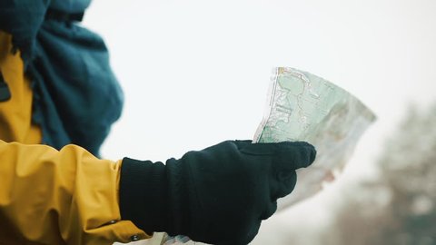 Man's hands in gloves holds the map, checking way, close-up. Beautiful mountains in winter time in the background