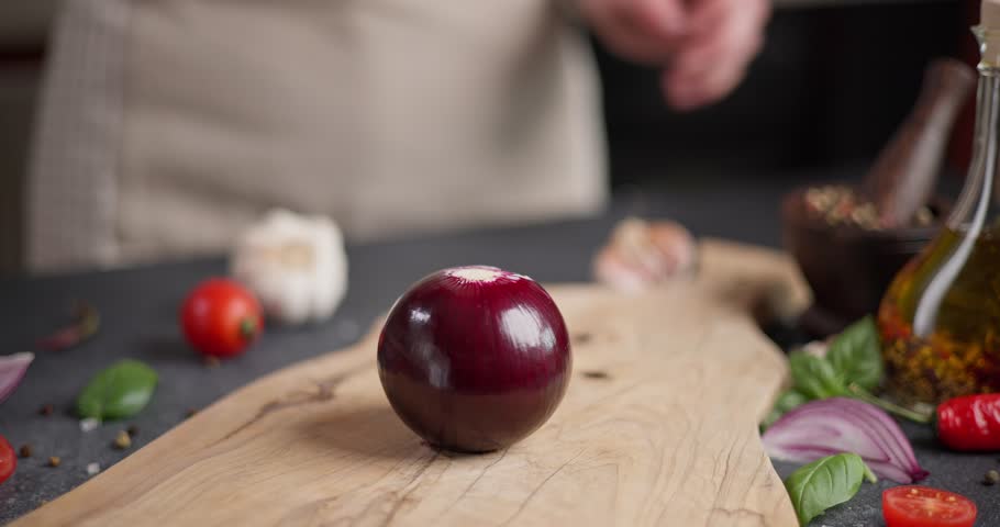 Woman cuts red Mars Onion on wooden cutting board at domestic kitchen