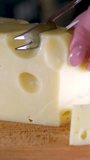 Female hands cutting cheese with a knife on a wooden cutting board. High quality 4k footage vertical video